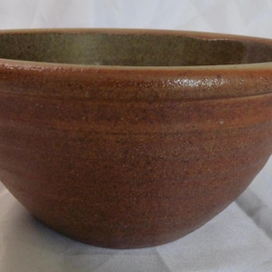 May include: A handmade, brown ceramic bowl with a spout. The bowl has a wide rim and a textured surface. The interior is a lighter brown color. The bowl is likely used for serving or mixing food.