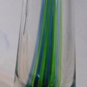 Könnte beinhalten: Eine klare Glasvase mit ausgestelltem Oberteil und rundem Boden. Vertikale Streifen aus blauem und grünem Glas sind im Inneren der Vase verschmolzen und bilden ein farbenfrohes, dekoratives Element. Die Vase ist etwa 20 cm hoch.