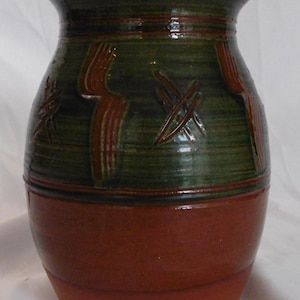 May include: A ceramic vase with a wide rim and a tapered base. The upper portion features a dark green glaze with carved, vertical, and cross-hatched brown patterns. The lower section is finished in a smooth, solid reddish-brown terracotta glaze.