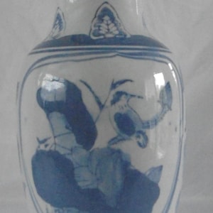 Puede incluir: Jarrón de cerámica blanca con diseños florales y de aves azules. El jarrón tiene un cuerpo redondeado y un borde acampanado. Los diseños azules incluyen aves, flores y otros elementos decorativos. Es un objeto decorativo.