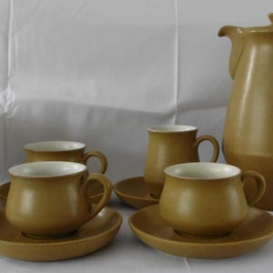 May include: A tan ceramic coffee set featuring a coffee pot, sugar bowl, and cups with saucers. The set has a simple, classic design with a matte finish. The cups and sugar bowl have white interiors.