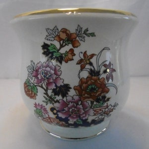 May include: A white ceramic vase with a gold rim and floral pattern. The vase features a design of pink, red, and blue flowers with green leaves on a white background.