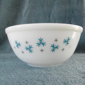 May include: White mixing bowl with a rounded shape. The bowl is decorated with teal and black starburst designs. The bowl is made of a thick, opaque material, and is suitable for kitchen use.