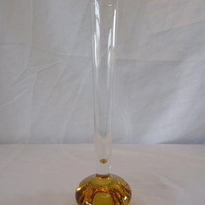 May include: A clear glass bud vase with a round, amber-coloured base. The base has a textured, bubbled surface.