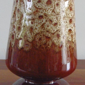 Puede incluir: Un jarrón de cerámica vintage con un diseño único. El jarrón presenta una base marrón oscuro que transiciona a un patrón texturizado marrón claro en la parte superior. El jarrón tiene una forma acampanada y se asienta sobre una base redonda.