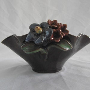 Puede incluir: Una maceta de cerámica marrón oscuro con un borde rizado y flores tridimensionales en tonos azules, rojos y verdes.