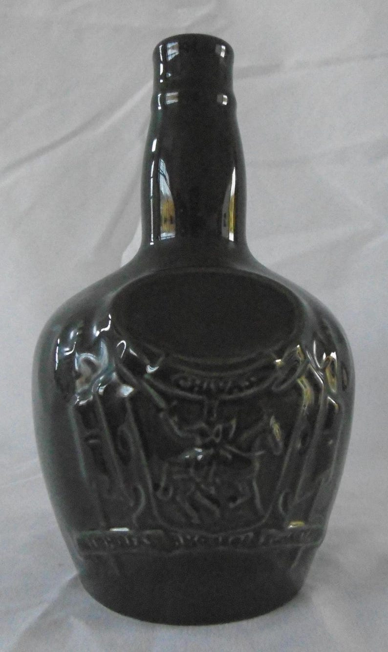 May include: A dark green ceramic bottle with a raised design of a knight on horseback. The bottle has a round body and a tall neck.