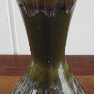 May include: A green and white ceramic vase with a unique hourglass shape. The vase has a glossy finish with a dark green base that fades to a lighter green and white at the top. The interior is white.