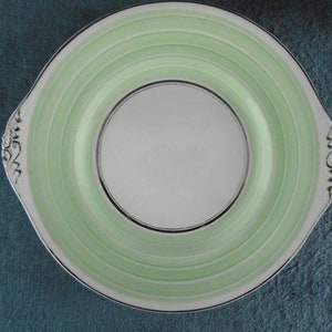 Puede incluir: Un plato de servir de cerámica blanca con círculos concéntricos verdes y plateados y asas decorativas.