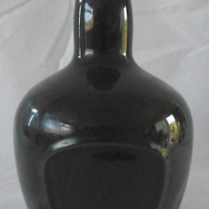 May include: A black ceramic bottle with a rounded body and a narrow neck. The bottle has a smooth, glossy finish and a rectangular label area.