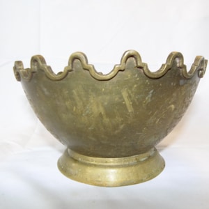 May include: A brass bowl with a scalloped rim and a decorative base. The bowl has a worn, antique finish.