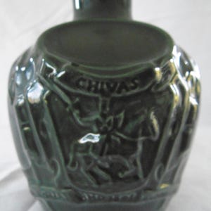 May include: A dark green ceramic decanter with a detailed embossed design featuring a crest and the word "CHIVAS".