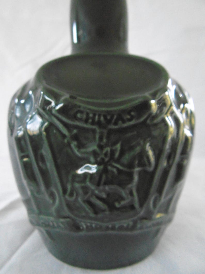 May include: A dark green ceramic decanter with a detailed embossed design featuring a crest and the word "CHIVAS".
