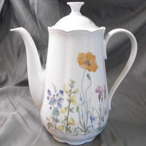 May include: White porcelain coffee pot with a lid and a curved handle. The pot is decorated with a floral design featuring an orange poppy and other colorful wildflowers. The pot has a long spout.