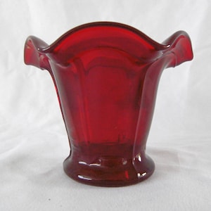 May include: A small, red glass vase with a ruffled rim. The vase is made of ruby red glass and has a slightly flared shape.