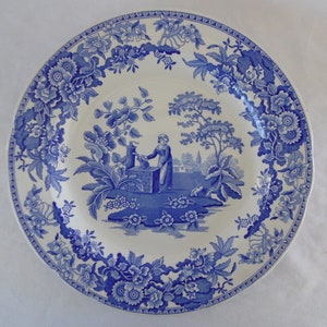 May include: A blue and white porcelain plate featuring a floral border and a central image of a woman drawing water from a well.