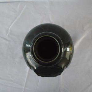 May include: A dark green ceramic vase with a wide opening and a smooth, rounded body. The vase has a glossy finish and a simple, elegant design.