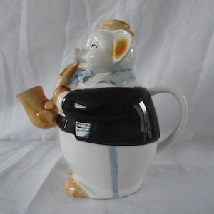 May include: A white ceramic teapot shaped like a pig wearing a black suit and a brown hat. The pig is holding a saxophone in its mouth. The teapot has a blue and white striped design on its body.