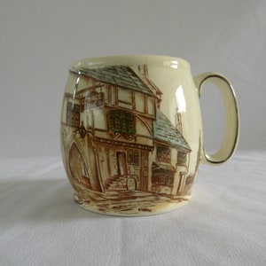 May include: A ceramic mug featuring a brown and white illustration of a building with the sign "George Inn". The mug has a rounded body and a handle.