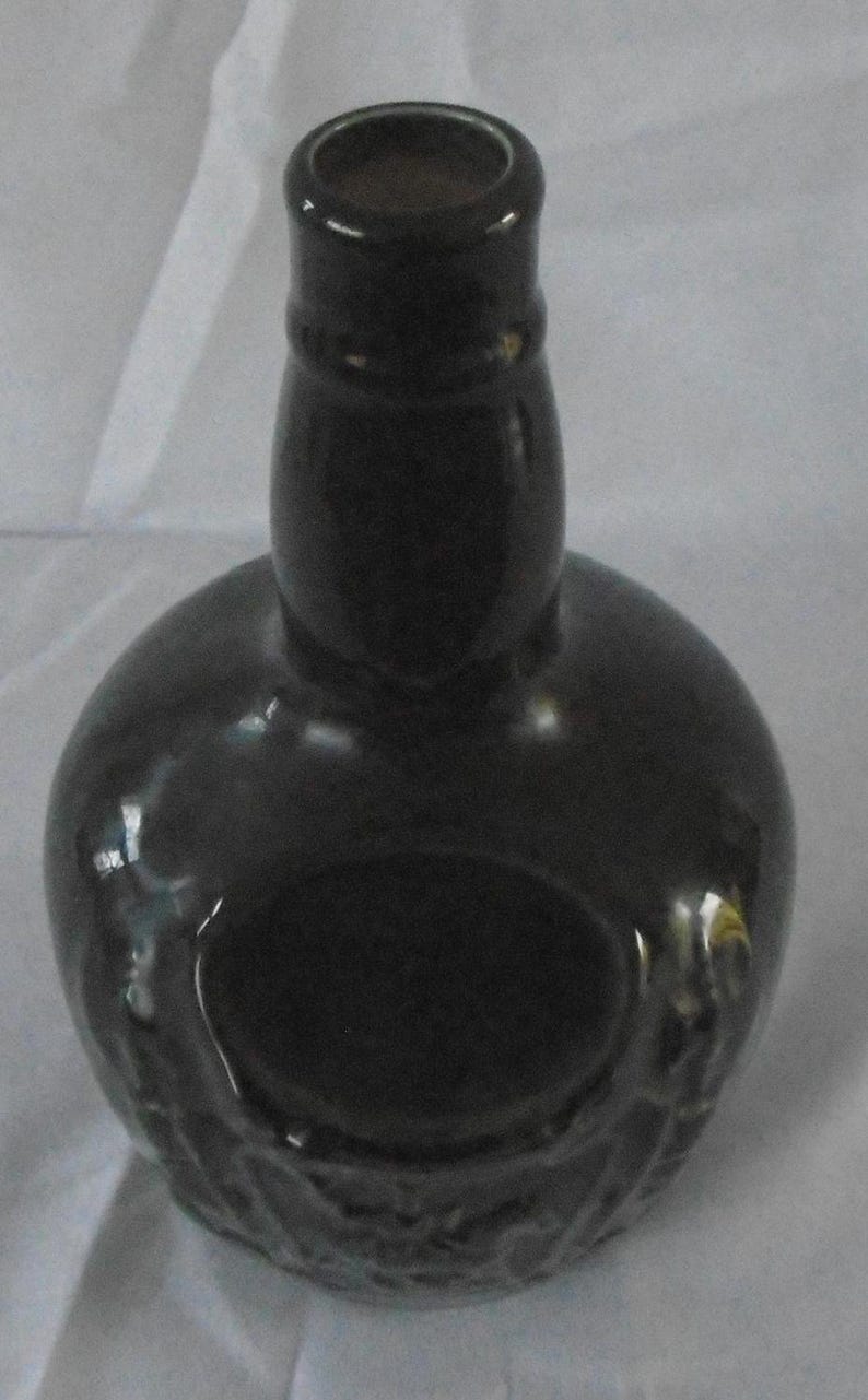 May include: A dark green glass bottle with a round body and a narrow neck. The bottle has a textured surface and a circular opening at the top.