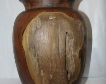May include: A dark brown wooden vase with a natural wood grain pattern. The vase has a wide mouth and a rounded body.