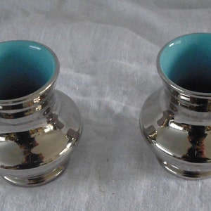 May include: Two silver ceramic vases with a light blue glaze inside. The vases have a rounded, bulbous shape.