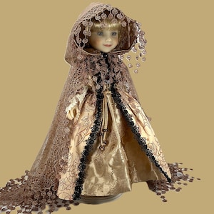 May include: A porcelain doll with blonde hair and blue eyes, wearing a long, flowing gown. The dress is a combination of gold and beige fabrics, accented with black lace trim and a brown lace cape. The doll's cape has a hood and is adorned with decorative embellishments.
