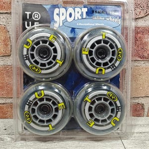 May include: Four clear inline skate wheels in a plastic package. Each wheel has a yellow and white design with the text "TRUE" and "SPORT". The package also has the text "4-Recreational Wheels".