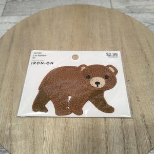 May include: A brown bear iron-on applique on a white card. The bear has a textured appearance with a light tan muzzle and black eyes. The card reads "IRON-ON" and "1 pc Appliqué".