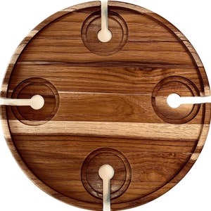 May include: A round wooden serving tray with four circular cutouts for glasses and four slots. The tray is made of light and dark brown wood, with a natural wood grain pattern. The cutouts are surrounded by a lighter-colored material.