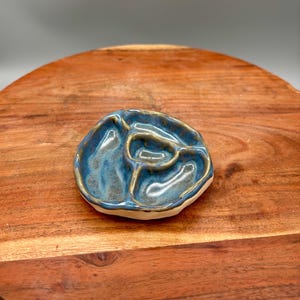 May include: A handmade ceramic serving dish with a unique, organic shape. The dish is divided into four sections and glazed in shades of blue and gold. The rim is a creamy white color.