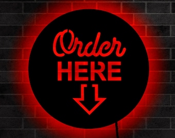 May include: A black circle sign with red neon lighting. The sign says "Order Here" with a red arrow pointing down.