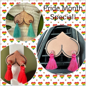 Puede incluir: Tres ambientadores de coche con forma de corazón con borlas. Los corazones son de color rosa, marrón y beige con contornos negros. Cada corazón tiene dos pequeños anillos plateados con borlas que cuelgan de ellos. Las borlas son de color turquesa, rojo y rosa. El texto "Pride Month Special!" está en el fondo.