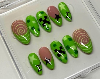May include: A set of ten almond-shaped press-on nails featuring a vibrant green and nude color palette. The designs include green and white checkered patterns, black pixelated shapes, white star outlines, and swirling pink and green spiral motifs.