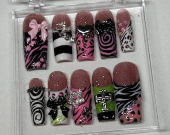May include: A set of ten false nails with different designs. The nails are pink, black, white, and green with glitter and rhinestones. Some nails have bows, stars, and crosses.