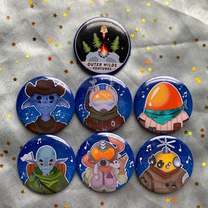 Puede incluir: Conjunto de siete botones redondos de pasador azul y blanco con varias ilustraciones. Los botones presentan una escena de fogata, un explorador espacial, una criatura con piel naranja, una criatura con piel azul, una criatura con piel verde, una criatura con piel amarilla y una criatura con piel naranja. Los botones tienen el texto "Outer Wilds Ventures" en uno de los botones.