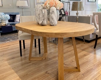 May include: A light wood oval dining table with a triangular base. The table is made of natural wood and has a light brown finish. The table is surrounded by white chairs.