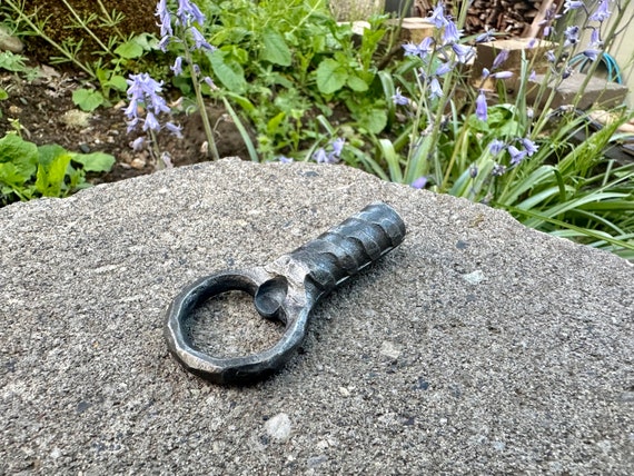 A blacksmith actually hammered rebar into a functional bottle opener — raw industrial material turned into a rugged, tactile bar tool.