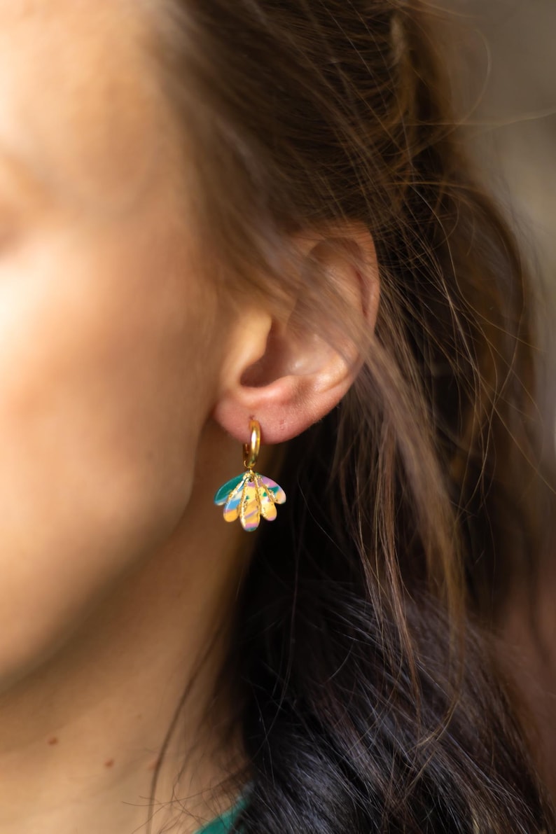 May include: Gold hoop earrings with a colorful, flower-shaped charm. The charm features a mix of pastel colors including yellow, pink, blue, and green. The earrings are a stylish accessory.