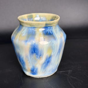 Peut inclure: Petit vase rond en céramique à large ouverture. Le vase présente un motif marbré de teintes bleues, blanches et jaunes. Le bord est de couleur beige clair. Le vase est probablement fait à la main et convient pour contenir des fleurs ou d'autres objets décoratifs.
