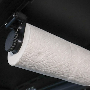May include: A black paper towel holder with a white paper towel roll attached. The holder is mounted to a black surface.