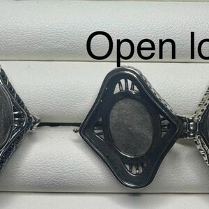 May include: Two silver-toned metal rings with a diamond-shaped face. One ring is closed, featuring a dark oval stone, while the other is an open locket revealing a hollow interior. The text 8 and Open locket are visible in the image.