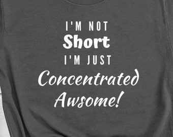 May include: A dark gray t-shirt with white text that reads "I'm not short I'm just concentrated awesome!" The shirt is laid out on a wooden surface with a pair of jeans and black sneakers.