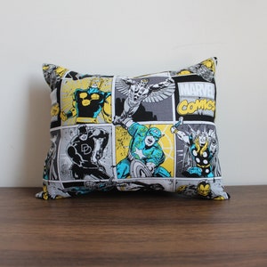 May include: A black pillow with a comic book pattern featuring Marvel Comics characters like Captain America, Daredevil, and Thor. The pillow has a yellow and gray background with the words "MARVEL COMICS" printed on it.