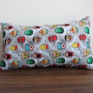 May include: A gray pillow with a repeating pattern of superhero faces in circles. The faces are in various colors, including red, blue, green, yellow, and black.