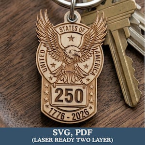 May include: Wooden keychain featuring a detailed eagle design with outstretched wings, the words "UNITED STATES OF AMERICA", and the number "250" with the years "1776-2026". The keychain is attached to a metal ring and is next to keys.