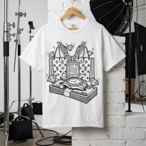 Puede incluir: Camiseta blanca con un diseño gráfico en blanco y negro de un bolso de lujo, un reloj de pulsera, diamantes y una pila de billetes de 100 €. El diseño incluye una cadena y un colgante de piedras preciosas.