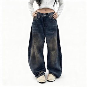 May include: Dark wash denim jeans with a wide, flared leg design. The jeans have a faded, distressed appearance with lighter patches. The model is wearing white platform shoes. The jeans have a button and zip closure.