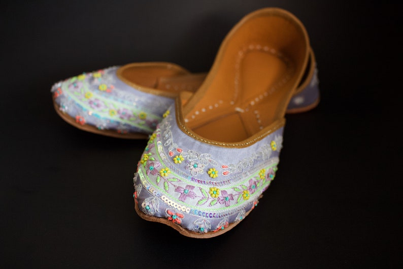 May include: A pair of light blue embroidered flat shoes with colourful floral designs and beaded accents.