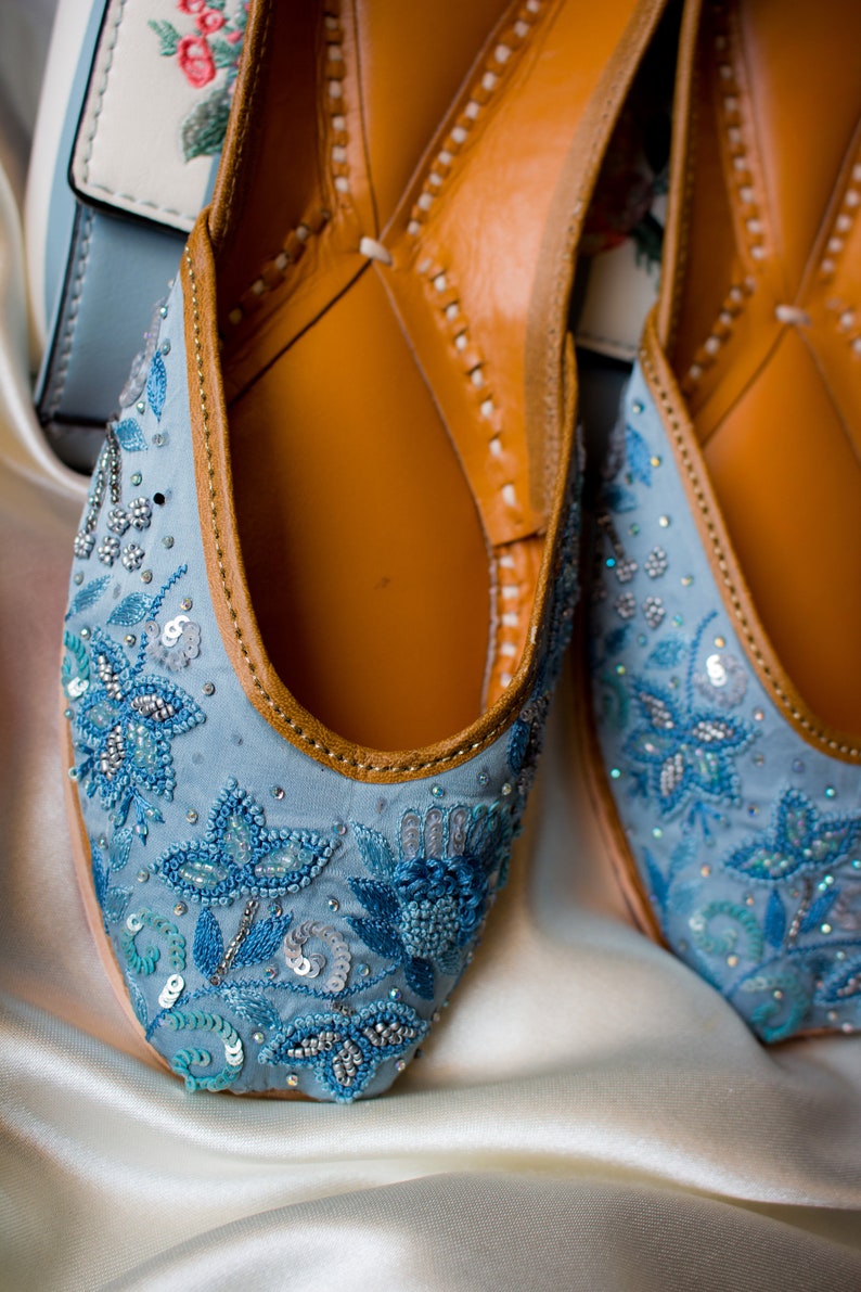 May include: A pair of blue embroidered flat shoes with leather soles. The shoes are decorated with silver and blue sequins and beads.